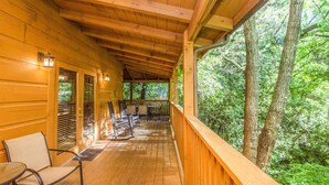 Eine Holzdar Terrasse mit überdachtem Bereich, möbliert mit Stühlen und einem Tisch, mit Blick auf ein bewaldetes Gebiet.