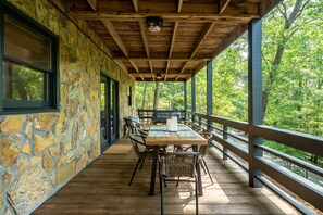Un espace extérieur abrité, doté d’un mur en pierre, d’une terrasse en bois et d’une table avec des chaises.