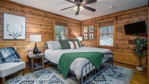 A cozy cabin bedroom with a bed, a chair, a lamp, and a television. - Mountain Crest Cottage Fabulous Fire Pit and 5 Minutes to Downtown Blue Ridge!  (Blue Ridge)