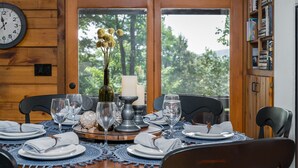 A dining table set with plates, glasses, and a centerpiece of flowers and candles. - Mountain Crest Cottage Fabulous Fire Pit and 5 Minutes to Downtown Blue Ridge!  (Blue Ridge)