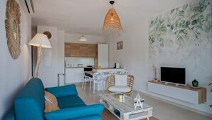 A modern living room with a blue sofa, a glass coffee table, and a TV on a wooden stand. - Playa Marina (Bastia)