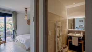 A modern bedroom with a large bed, a bathroom with a sink and mirror, and a view of the outside. - Playa Marina (Bastia)