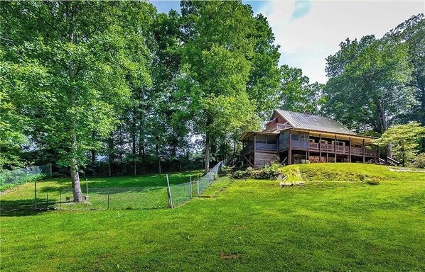 Un chalet rustique aux murs en bois, entouré d’une végétation luxuriante et doté d’une cour clôturée.