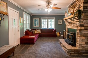Un salon avec une cheminée en pierre, un canapé rouge, un ventilateur de plafond et une grande fenêtre.