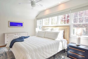 A bedroom with a bed, a dresser, a TV, and a window with a view of trees.