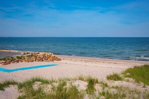 A beach with a clear sky, a sandy area with rocks, and a blue mat.