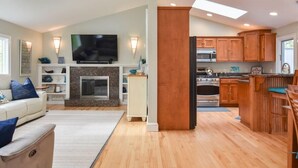 Una sala de estar moderna con chimenea, televisor y una zona de cocina con armarios de madera y una barra.