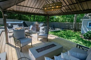 Eine überdachte Terrasse im Freien mit Feuerstelle, Sitzgelegenheit und Grill.