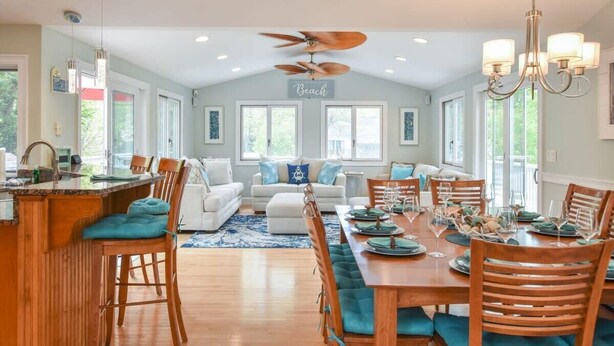Un comedor espacioso con un ventilador de techo alto, una zona de cocina con barra y una sala de estar con sofá y un cartel que dice "Beach".