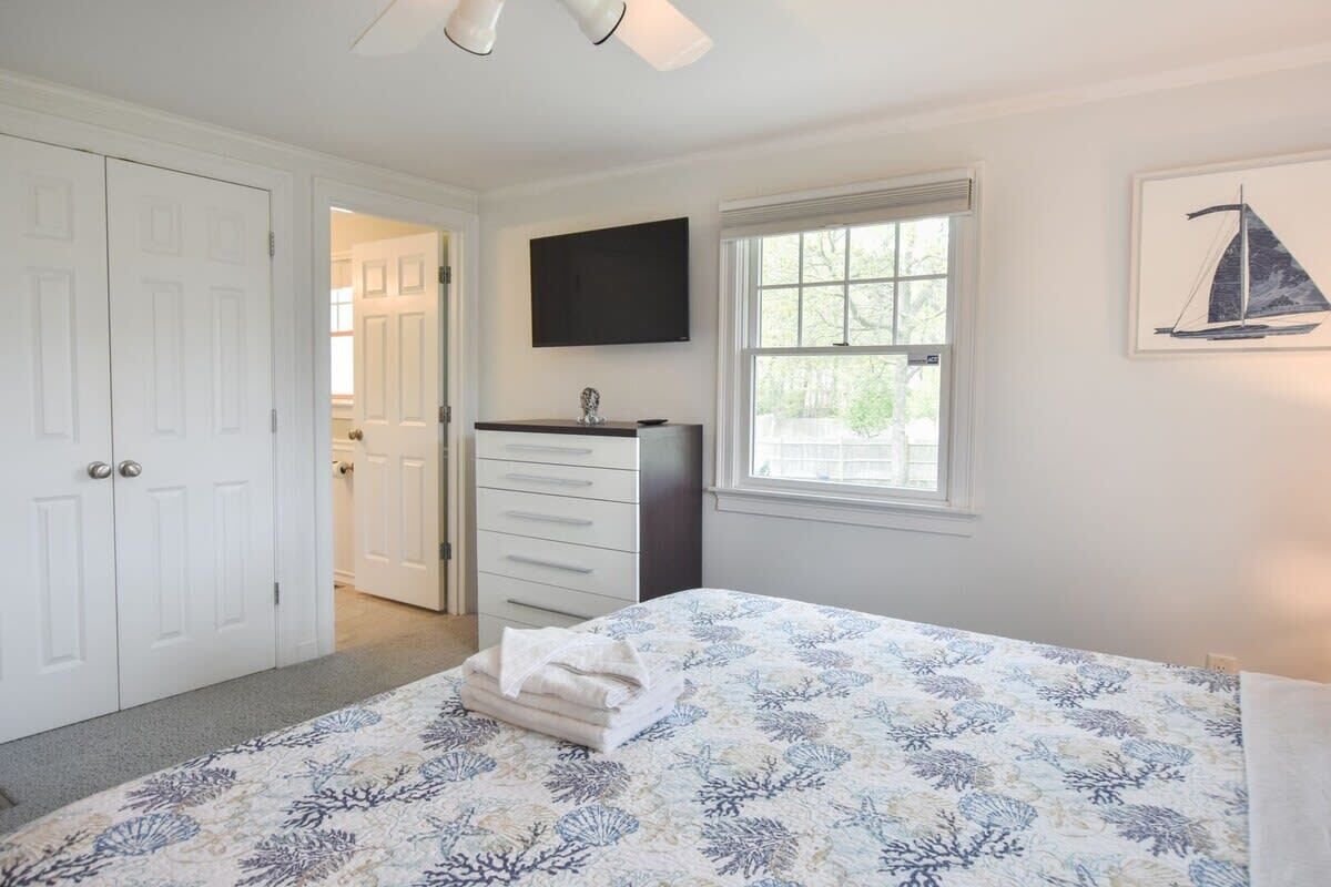 Un dormitorio con cama, cómoda, televisor, ventana y puerta.