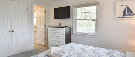 Un dormitorio con cama, cómoda, televisor, ventana y puerta.