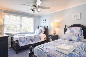 Ein Schlafzimmer mit zwei Betten, einem Deckenventilator, einem Fenster mit Jalousien und einer Wand mit einem gerahmten Bild.