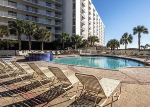 Un espace piscine d’hôtel avec des chaises longues, une piscine et un immeuble à plusieurs étages en arrière-plan.
