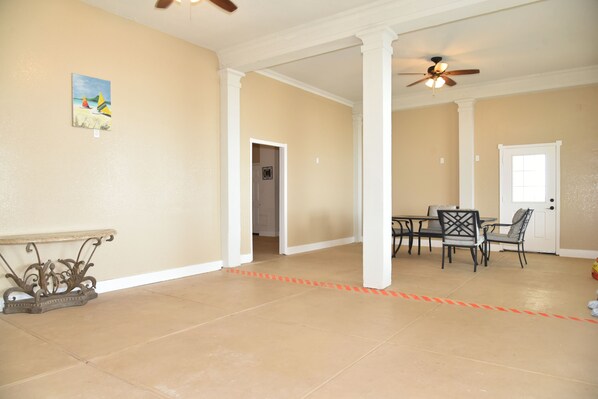 A spacious room with beige walls, a dining area with a table and chairs, a ceiling fan, and a door leading to another room. - SUNBATHERBYTHESEA beautiful private beach front villa. Perfect place for wedding (Galveston)