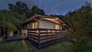 Una casa moderna con techo inclinado, terraza de madera y un pequeño patio.