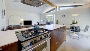 Una cocina moderna con estufa a gas, armarios de madera y un comedor con mesa y sillas de vidrio.