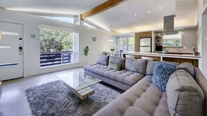 Una sala de estar moderna con un sofá gris, una mesa de centro de vidrio y vistas al exterior.
