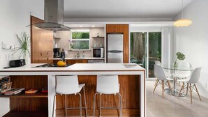 Una cocina moderna con una isla central, taburetes de bar y un comedor con mesa de vidrio y sillas.