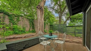 Un patio con una mesa redonda y cuatro sillas, una planta en maceta y el tronco de un árbol.