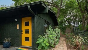 Un pequeño edificio con puerta amarilla, rodeado de cactus y un sendero de piedra.
