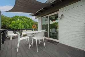 An outdoor patio with white plastic chairs and a table, a dark canopy, and a white brick wall with a sliding glass door.