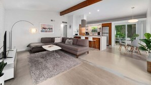 Un salon moderne avec un canapé d’angle, une table basse et un coin repas avec des chaises blanches.