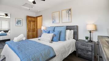Un dormitorio con cama, mesitas de noche, ventilador de techo y obras de arte en las paredes.