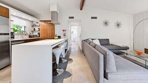Une cuisine moderne dotée d’un îlot central, un coin repas avec un canapé et un salon avec une table basse en verre.