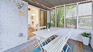 Un patio couvert avec une table et des bancs blancs, un pot de fleurs et une vue sur l’extérieur.