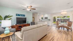 A living room with a beige sofa, a television, and a ceiling fan. - Coastal Cottage / 1 Mile to Hobe Sound Public Beach (Hobe Sound)