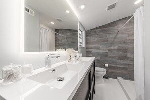 Une salle de bain moderne avec un grand miroir, deux lavabos, des toilettes et un espace douche.