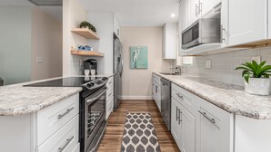 A modern kitchen with white cabinets, granite countertops, stainless steel appliances, and a patterned rug. - Coastal Cottage / 1 Mile to Hobe Sound Public Beach (Hobe Sound)