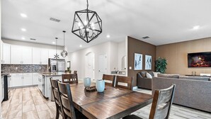 A modern kitchen with white cabinets, a central island, and a dining area with a wooden table and chairs.