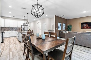 Una cocina moderna con armarios blancos, una isla central y un comedor con una mesa y sillas de madera.