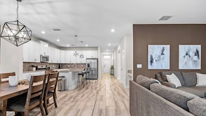 A modern kitchen with white cabinets, a central island, and a dining area with wooden chairs.