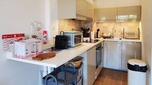 Eine kleine Küche mit Mikrowelle, Toaster, Spüle und Schränken. Auf der Arbeitsfläche stehen Kartons und Küchenutensilien.
