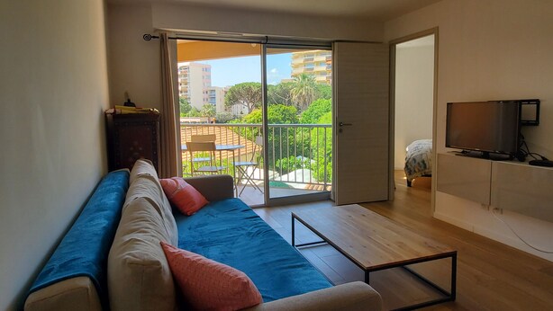 Ein Wohnzimmer mit einer Couch, einem Fernseher und einem Balkon mit Tisch und Stühlen.