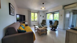 A living room with a sofa, armchairs, a coffee table, and a TV. There are windows with curtains, a ceiling fan, and an air conditioning unit. - Port FREJUS 3 air-conditioned rooms 80m2 4 people near beaches and nature base (Fréjus)
