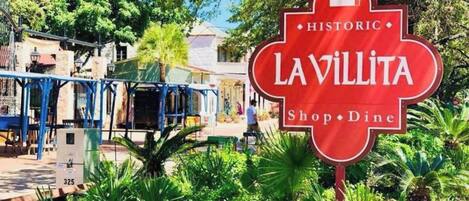A red sign with 'LAVILLITA Shop · Dine' and 'HISTORIC' written on it, surrounded by greenery and a building in the background.