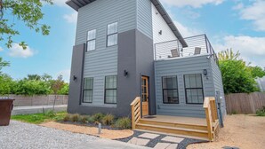 A modern two-story house with a grey exterior, a wooden front door, and a small porch with steps. - Experience Modern Luxury! 3br/2.5ba Home Near DT (San Antonio)