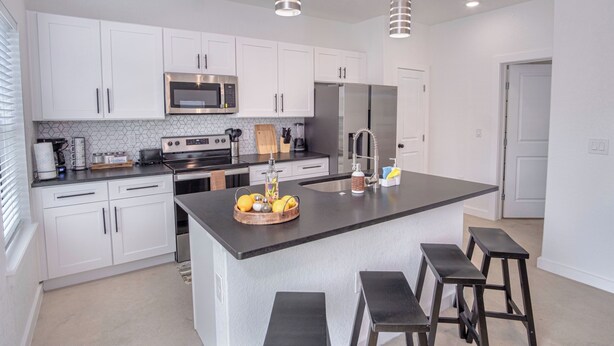 A modern kitchen with white cabinets, stainless steel appliances, and a central island with stools. - Experience Modern Luxury! 3br/2.5ba Home Near DT (San Antonio)