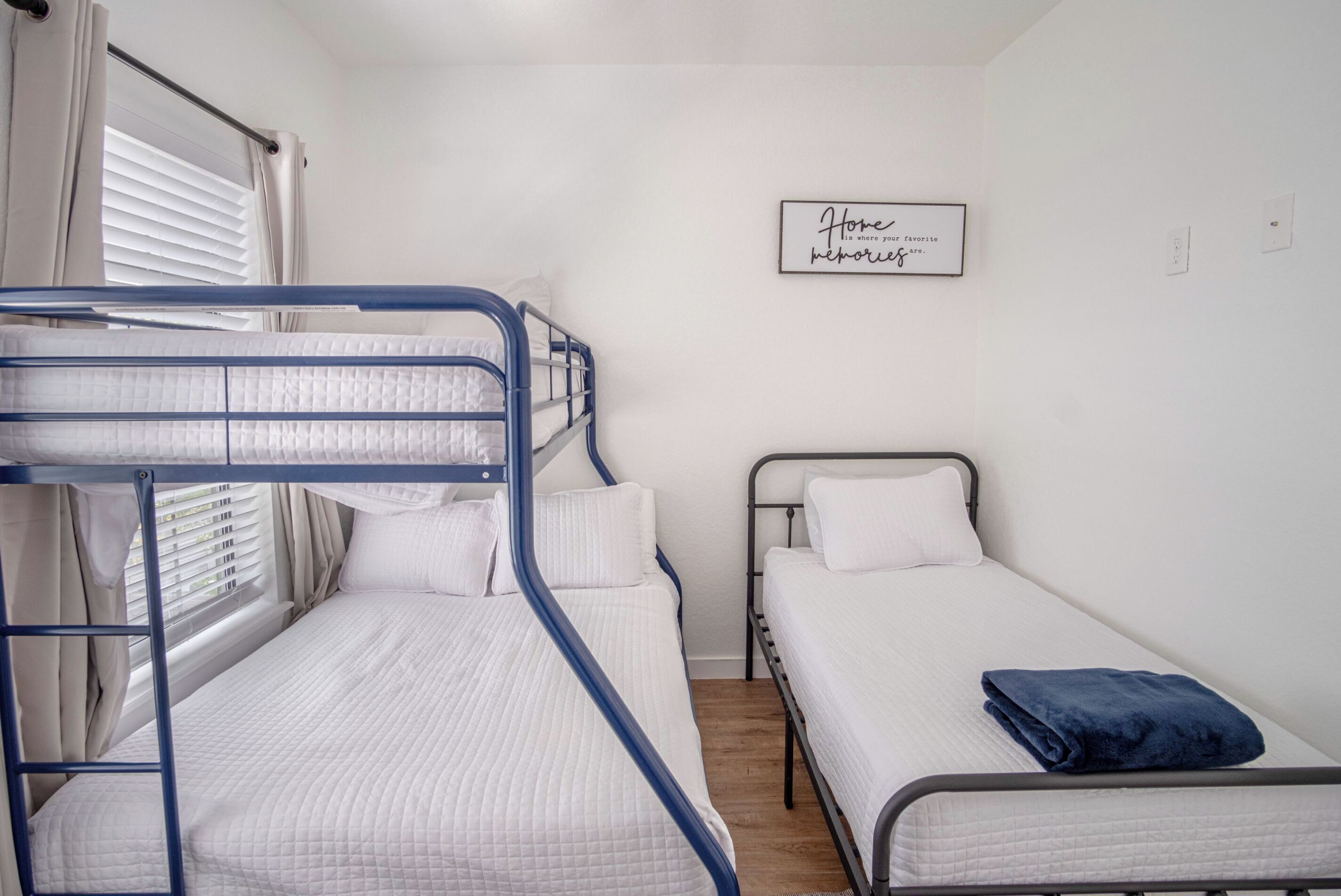 Une chambre de dortoir avec des lits superposés, un lit simple, une fenêtre avec des rideaux et un panneau mural.