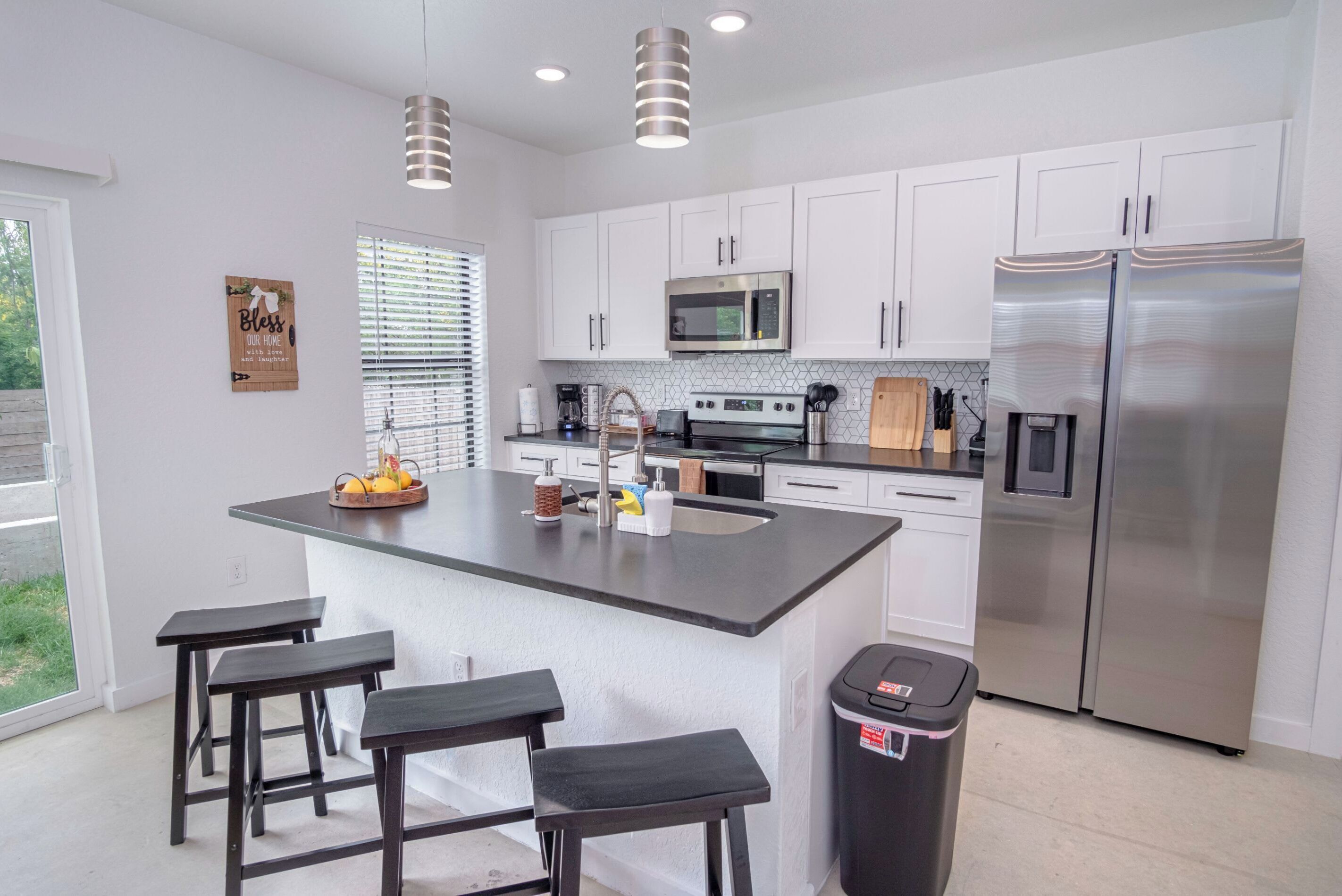 A modern kitchen with white cabinets, a stainless steel refrigerator, a microwave, and a large island with bar stools.