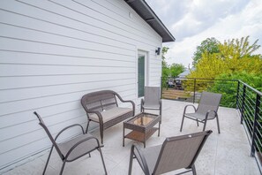 Un balcon agrémenté de meubles en osier, d’une table en verre et offrant une vue sur un jardin et des arbres.