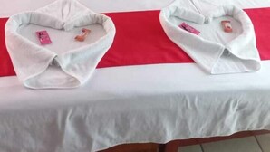 Uma cama com cabeceira vermelha, roupa de cama branca e duas toalhas em formato de coração sobre a cama.