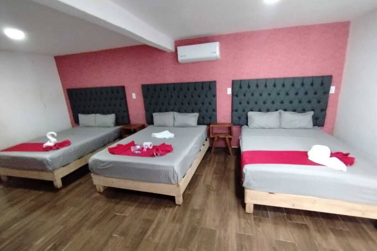 A hotel room with three single beds, each with a red towel and a white swan decoration. The room has a red and white color scheme with a modern design.