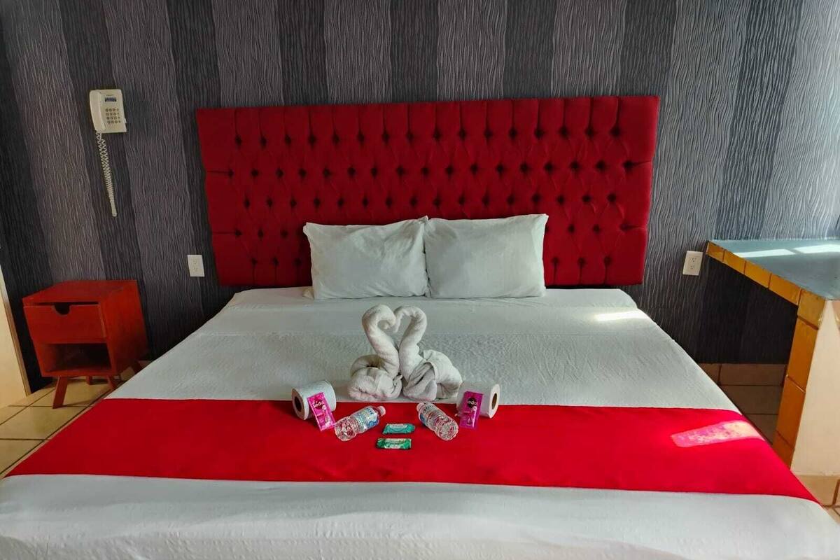 A hotel room with a red tufted headboard, white bedding, and a red accent on the bedspread.