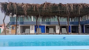 Piscina com espreguiçadeiras e área coberta com telhado de palha.