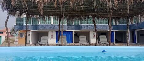 Piscina com espreguiçadeiras e área coberta com telhado de palha.