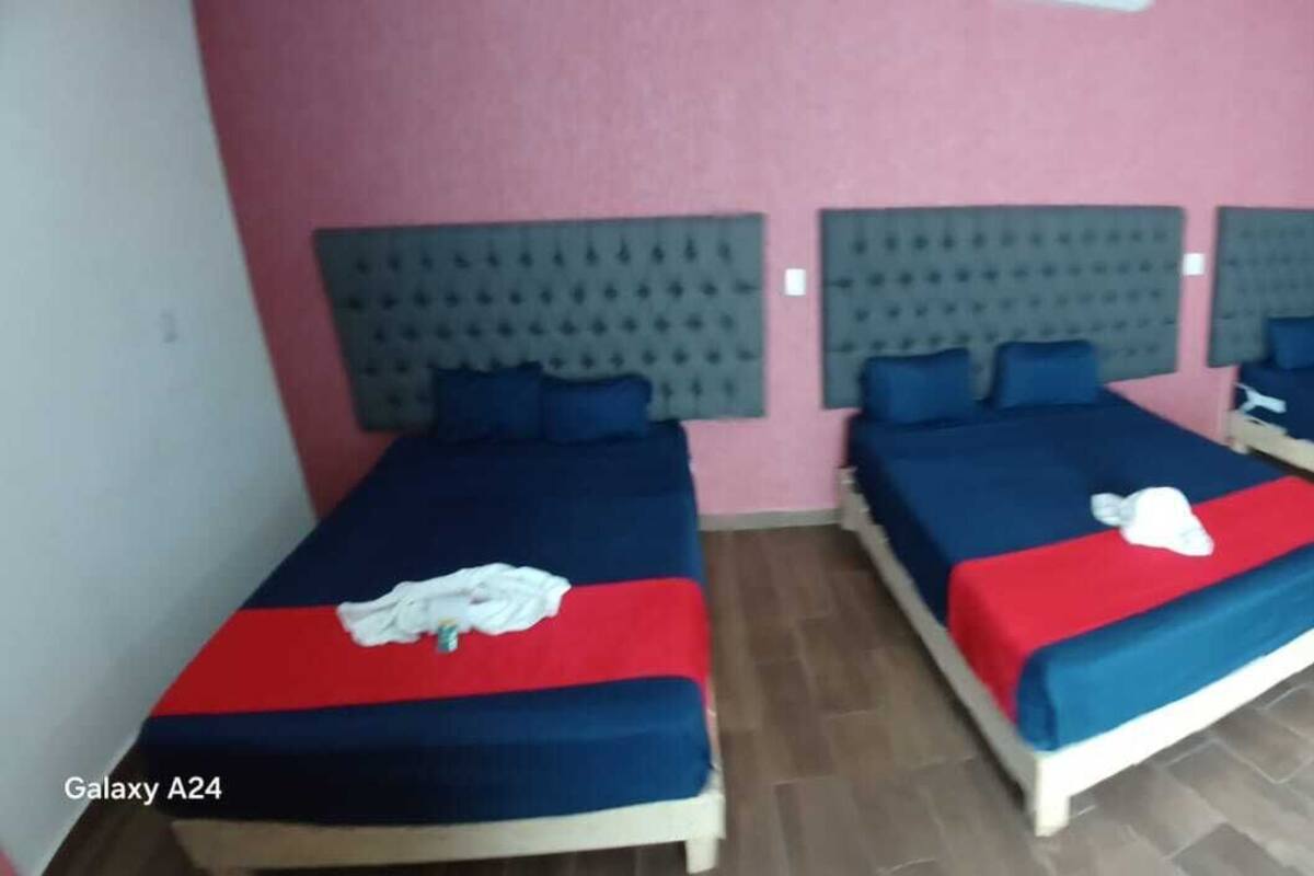 A hotel room with three beds, a blue sofa, and a TV mounted on the wall.